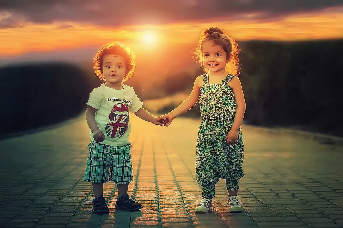 Two young children holding hands in warm sunlight